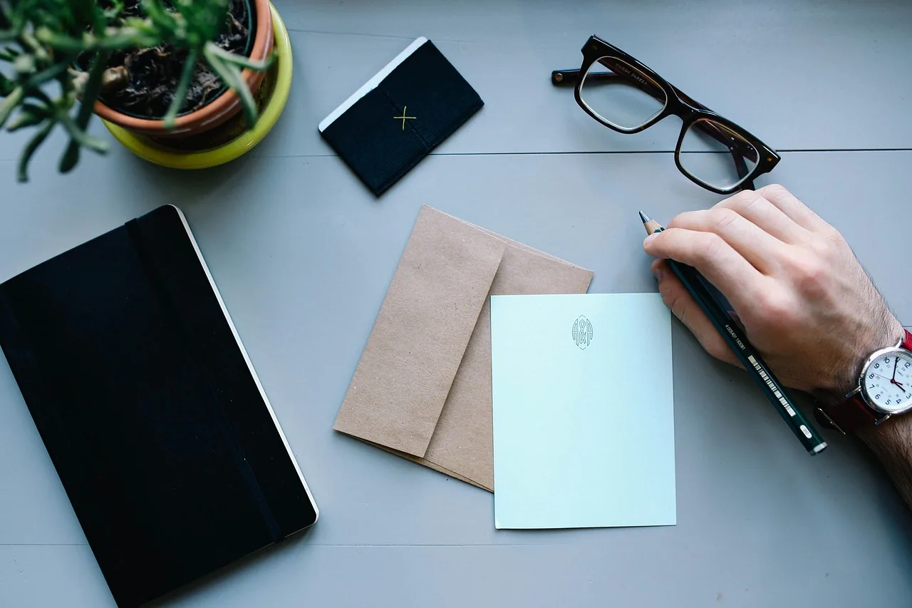 A hand writing notes at a quiet desk with a notebook and glasses